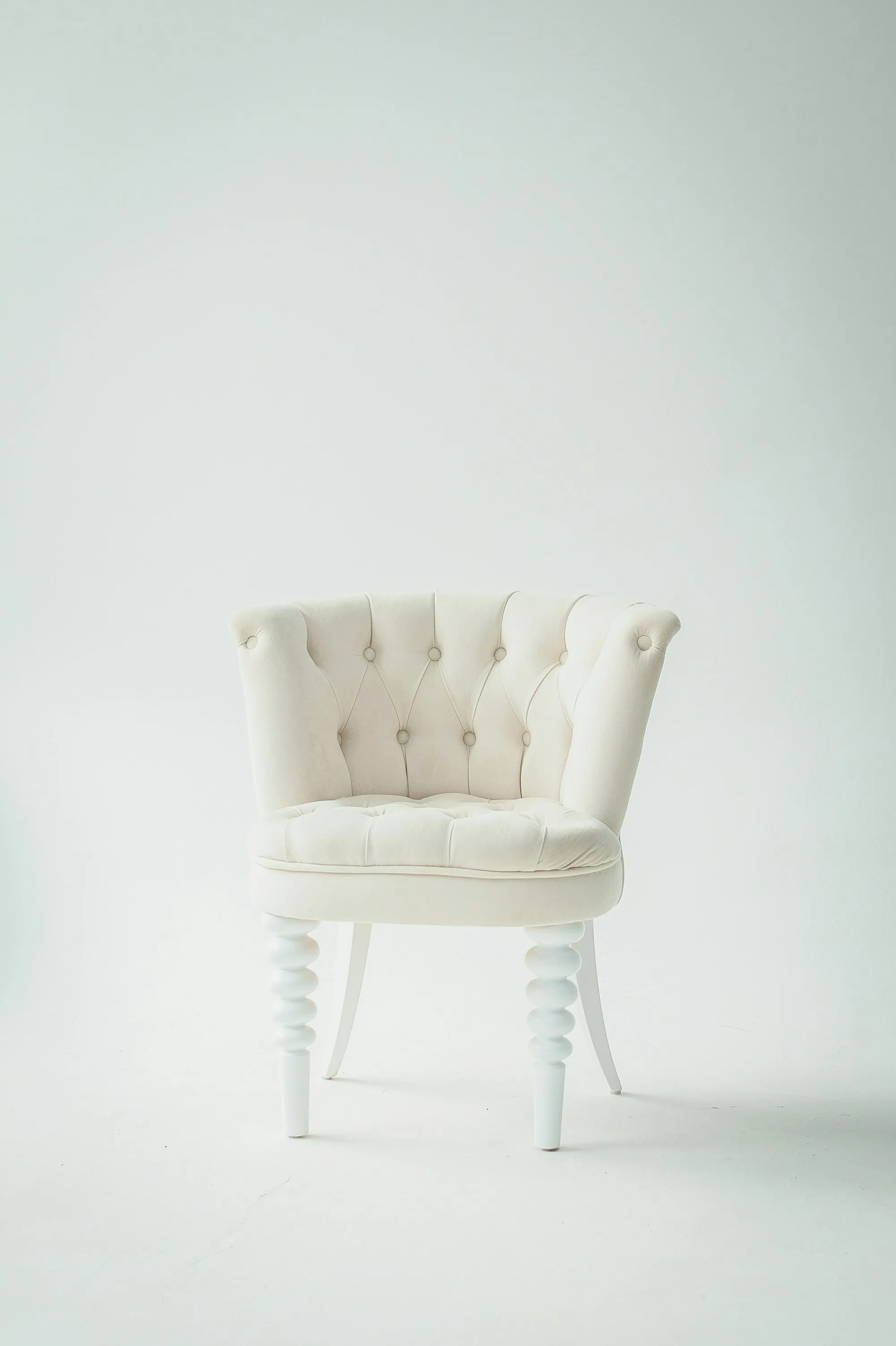 A white tufted antique chair against a pale wall